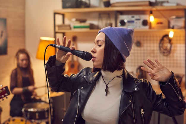 Chica morena cantando en el micrófono contra sus amigos tocando instrumentos musicales