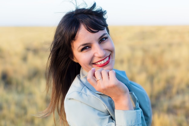 Chica morena con una chaqueta azul en un campo con hierba amarilla.