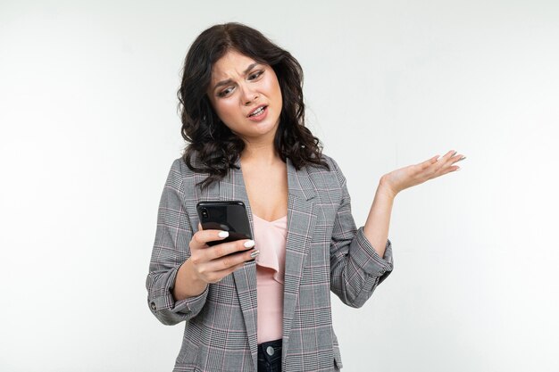 Chica morena en una chaqueta gris con un teléfono en sus manos se comunica sobre un blanco aislado