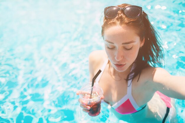 Chica morena con cócteles relajantes en la piscina