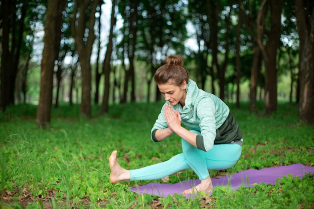 Chica morena delgada hace deporte y realiza posturas de yoga hermosas y sofisticadas en un parque de verano.