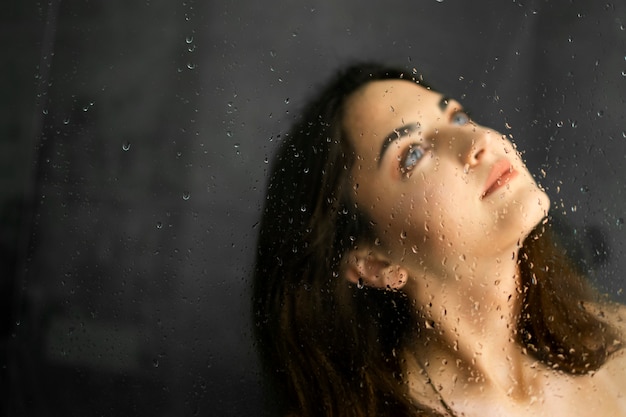 Chica morena en la ducha. Gotas de agua en la mampara de la ducha. Retrato