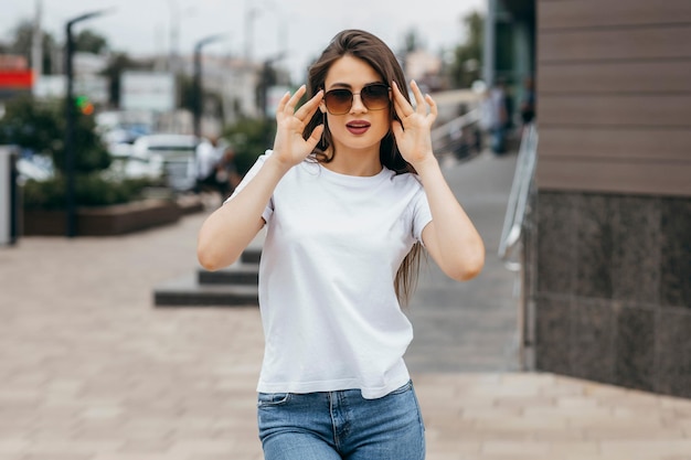 Chica morena elegante con camiseta blanca y gafas posando contra el estilo de ropa urbana de la calle