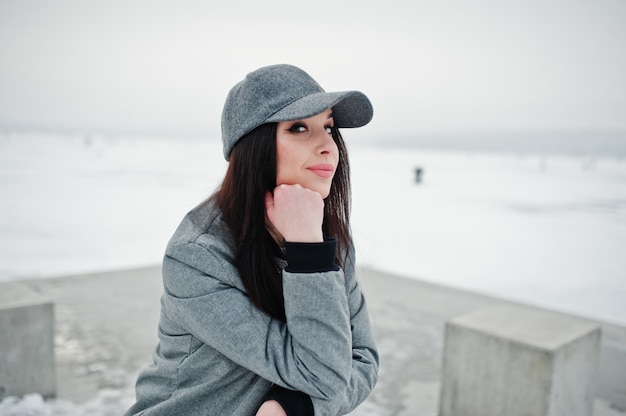 Chica morena elegante con gorra gris en día de invierno.