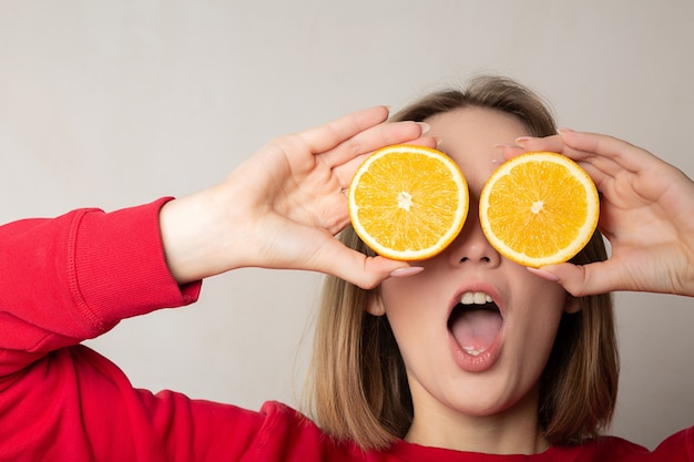 Chica morena emocional posando con una media naranja que cubre los ojos contra la pared blanca
