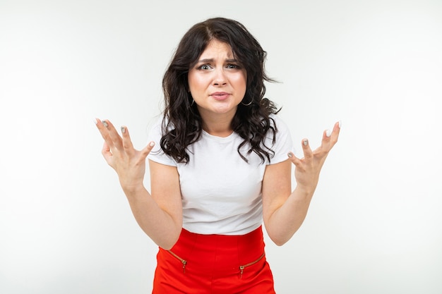 Chica morena indignada en una camiseta blanca harta de un fondo blanco de estudio.