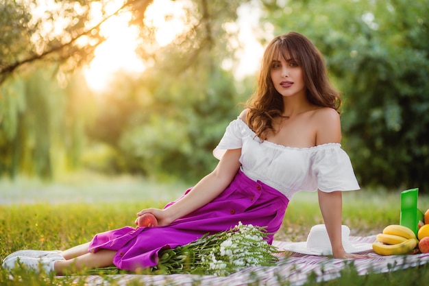 Chica morena joven con el pelo rizado en un picnic en un parque de verano Luz solar suave al atardecer