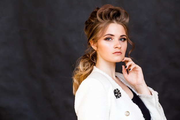 Chica morena de moda posando sobre un fondo negro en una elegante chaqueta blanca con un broche en forma de rombo de flores