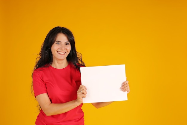 Una chica morena con el pelo largo en una camiseta roja sostiene una hoja blanca de papel amarillo en sus manos