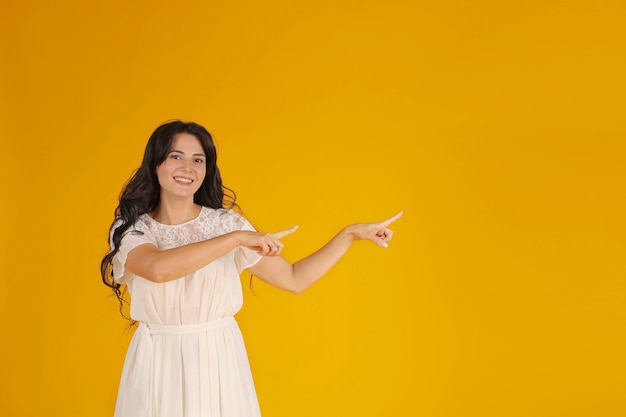 una chica morena con el pelo largo con un vestido blanco muestra la dirección con sus manos