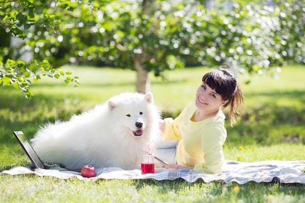 Una chica morena con un perro blanco en la naturaleza.