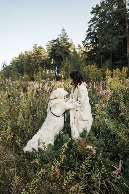 Chica morena con perro golden retriever blanco en el campo