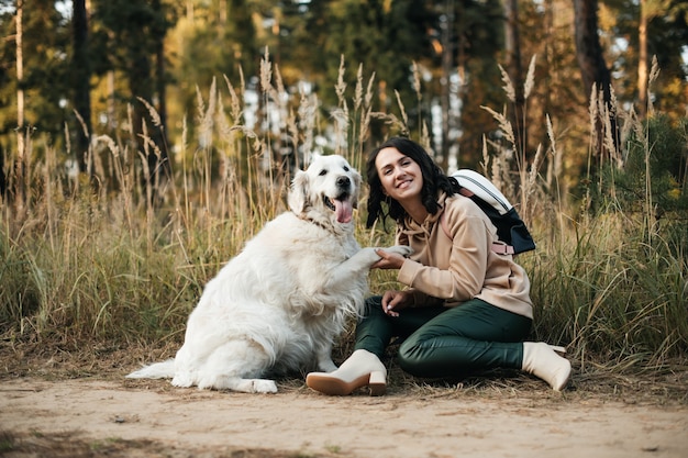 Chica morena con perro golden retriever blanco en el sendero del bosque