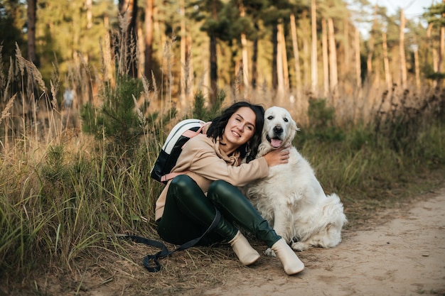 Chica morena con perro golden retriever blanco en el sendero del bosque
