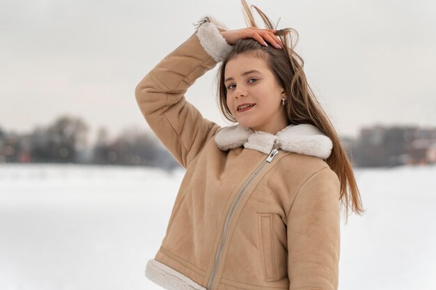 Chica morena posa maravillosamente en un abrigo de piel de oveja beige de moda decorado con piel blanca sobre fondo de claro nevado