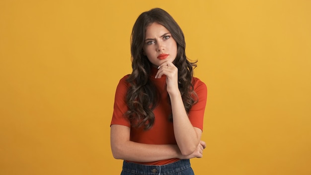 Una chica morena seria y pensativa con la parte superior roja mirando enojada a la cámara sobre un fondo colorido Expresión de pensamiento