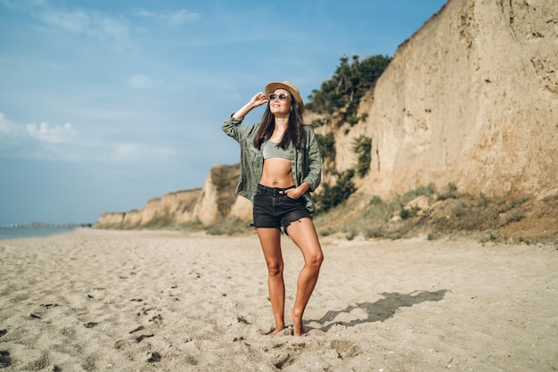 Chica morena con sombrero relajante en la playa con rocas