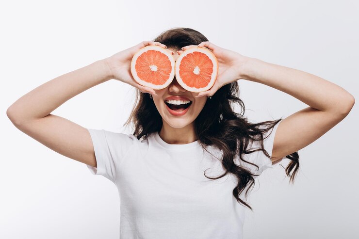 Chica morena sonriente que cubre sus ojos con mitades de pomelo