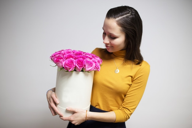 Chica morena sosteniendo un ramo de rosas rosadas brillantes en una caja