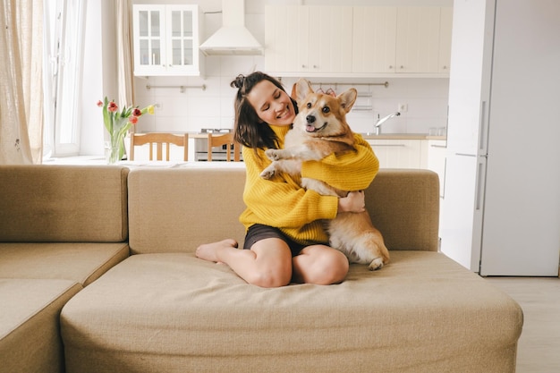 Foto una chica morena con un suéter amarillo abraza a un perro sentado en el sofá