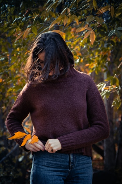 Chica morena con un suéter marrón pone hojas amarillas en el bolsillo de los pantalones vaqueros