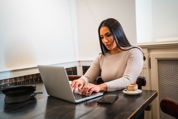 Chica morena teletrabajo en una cafetería con portátil