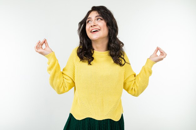 Chica morena tranquila en un suéter amarillo y falda verde atrapa la paz en un blanco