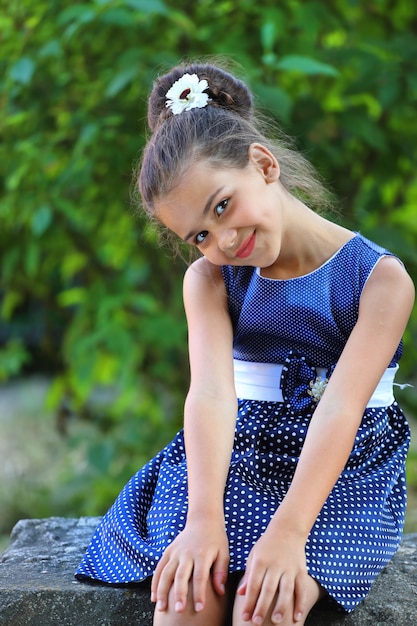 Una chica morena con un vestido de lunares azul sentada en el parque en verano. Foto de alta calidad