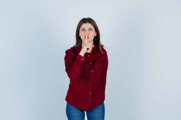 chica mostrando gesto de silencio en camisa burdeos y mirando seria.