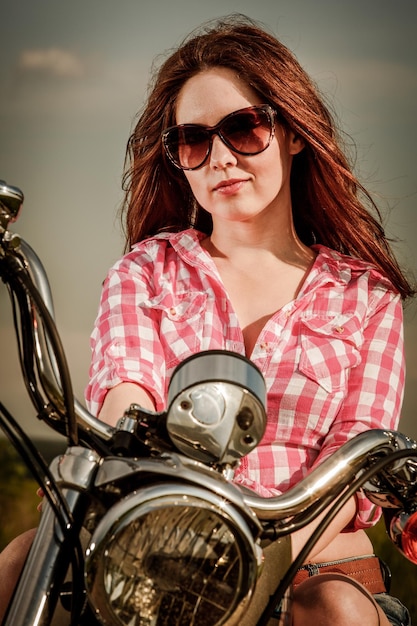 Chica motera con gafas de sol sentada en motocicleta