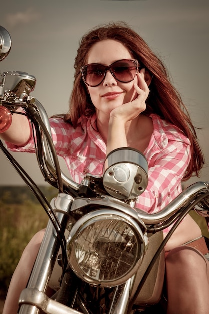 Chica motera con gafas de sol sentada en motocicleta