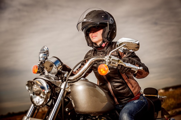 Chica motociclista en una chaqueta de cuero y casco en una motocicleta