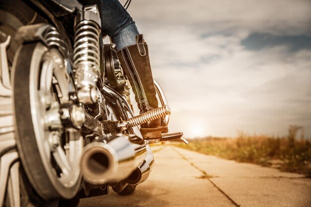 Chica motorista montando en una motocicleta. Vista inferior de las piernas con botas de cuero.