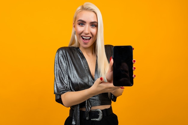 La chica muestra una pantalla de teléfono en blanco con un diseño en una pared naranja