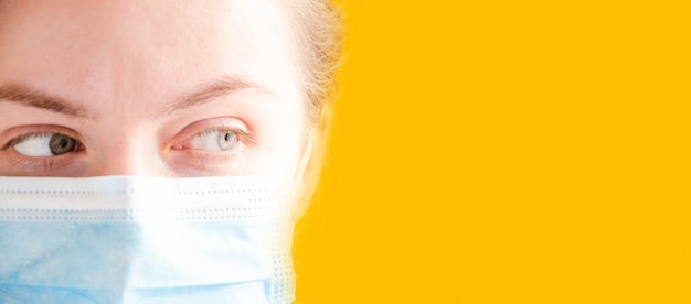 Foto chica, mujer con una máscara médica azul, de lado. chica sobre un fondo amarillo. lugar para el texto. copia espacio. covid-19