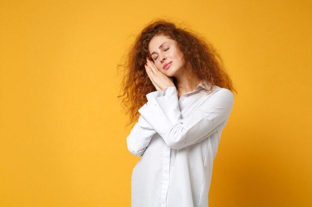 Chica de mujer pelirroja joven relajada en camisa blanca casual posando aislada en la pared naranja amarilla