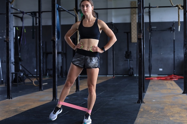 Chica musculosa y fuerte haciendo ejercicios con goma de fitness en el gimnasio.