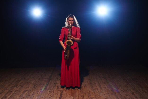 Chica músico con un vestido rojo con un saxofón en el escenario