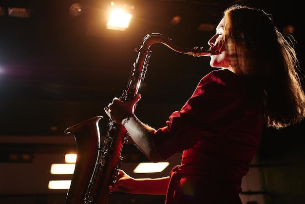 Chica músico con un vestido rojo con un saxofón en el escenario