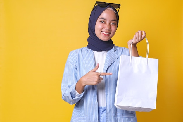 Chica musulmana alegre con estilo casual y gafas de sol apuntando a bolsas de compras