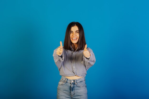 Una chica muy feliz en jeans y camisa a rayas azules muestra un signo genial.