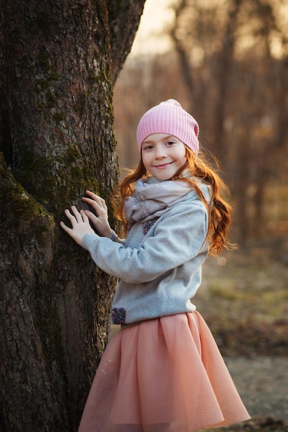 Chica muy sonriente con pelo rojo y pecas cerca de un árbol en primavera u otoño