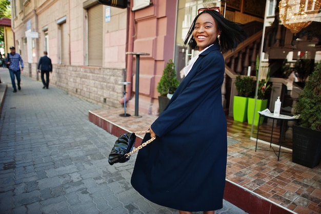 Chica de negocios chic africana en abrigo con bolso Retrato callejero de moda de mujer afroamericana