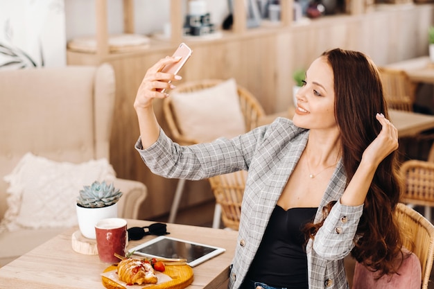 Una chica de negocios está sentada en un café y tomando un selfie