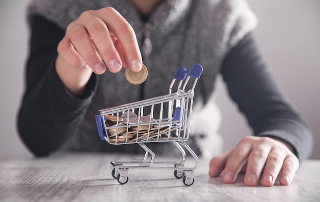 Chica de negocios poniendo monedas al carrito de compras. Concepto de compras