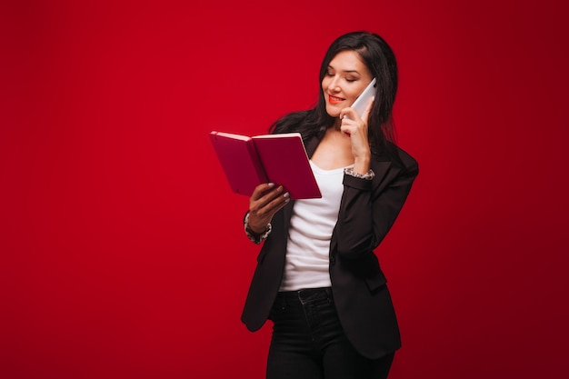 Chica de negocios en un traje hablando por teléfono y mirando portátil. Sobre fondo rojo