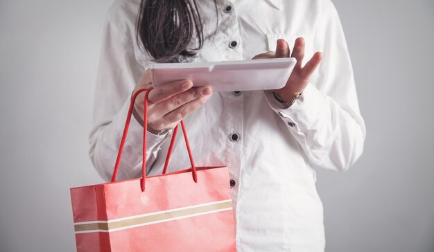 Chica de negocios usando tableta y sosteniendo el bolso de compras.