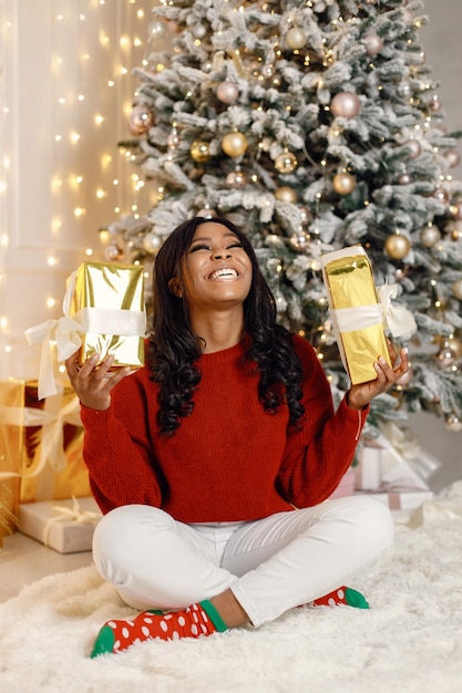 Chica negra cerca del regalo de apertura del árbol de Navidad en casa