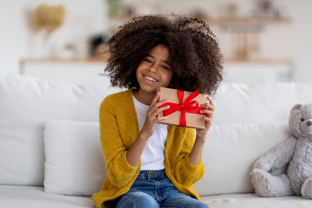 Chica negra feliz sentada en el sofá con regalo