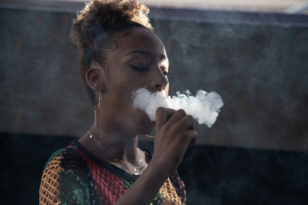 Chica negra fumando con un vapor